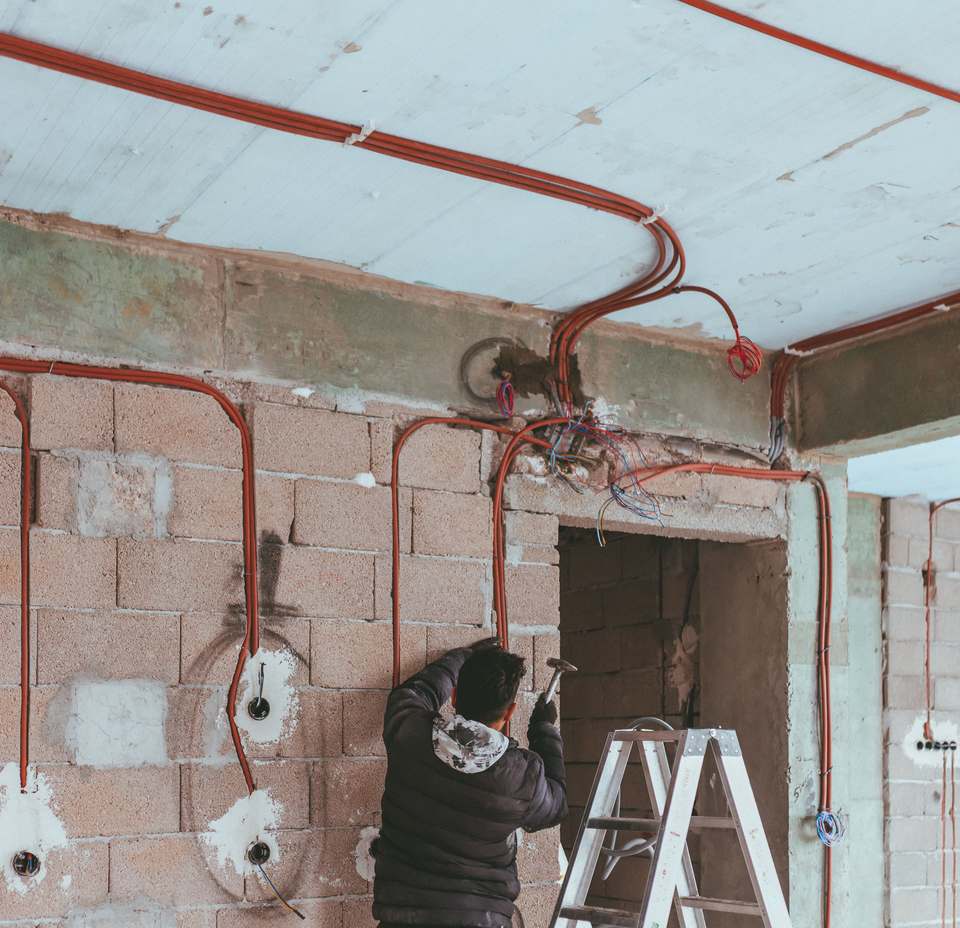 Electrician trăgând tuburi de protecție portocalii pe pereții unei locuințe aflate în renovare